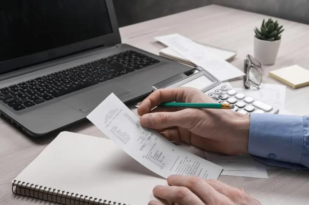 Persona usando una calculadora y tomando notas junto a documentos de trabajo